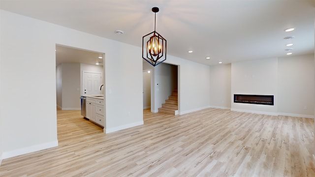 unfurnished living room featuring a notable chandelier, light hardwood / wood-style floors, and sink