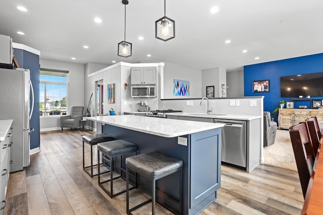 kitchen featuring sink, light hardwood / wood-style floors, pendant lighting, a kitchen island, and appliances with stainless steel finishes