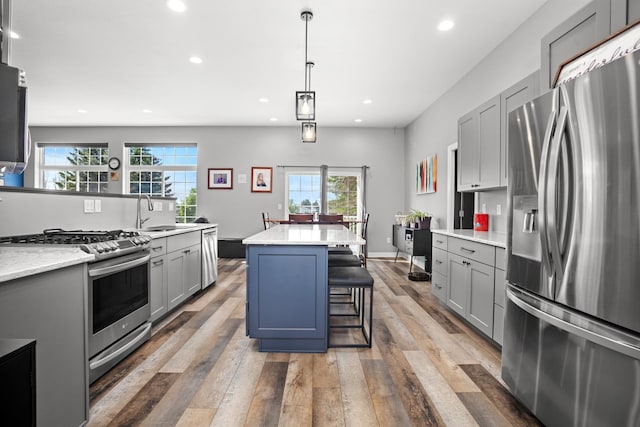 kitchen with stainless steel appliances, sink, gray cabinets, a kitchen island, and dark hardwood / wood-style floors