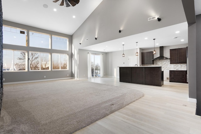 living room featuring ceiling fan, a towering ceiling, and light wood-type flooring