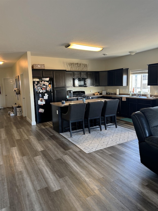 kitchen with a breakfast bar, a center island, black appliances, and wood-type flooring