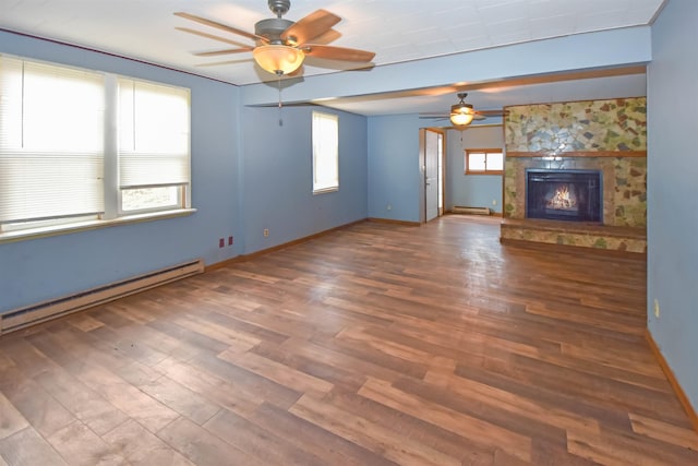 unfurnished living room featuring baseboard heating, a stone fireplace, a wealth of natural light, and hardwood / wood-style floors