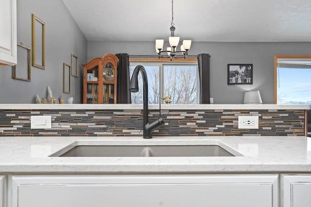 details featuring white cabinets, a notable chandelier, sink, decorative light fixtures, and backsplash