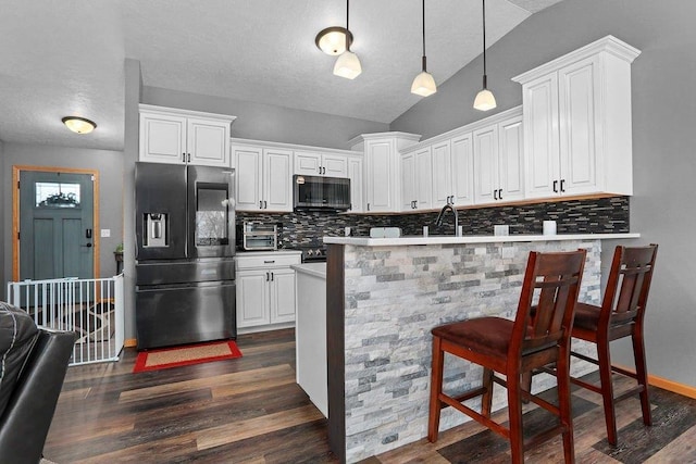 kitchen featuring a kitchen breakfast bar, vaulted ceiling, appliances with stainless steel finishes, white cabinetry, and backsplash