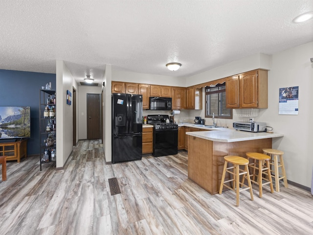 kitchen featuring kitchen peninsula, a textured ceiling, black appliances, a breakfast bar, and sink