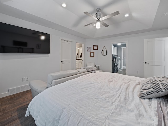 bedroom with ensuite bathroom, ceiling fan, a tray ceiling, dark hardwood / wood-style flooring, and washer / clothes dryer