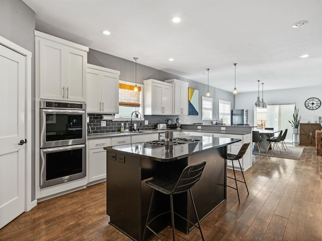 kitchen featuring a center island, white cabinetry, stainless steel appliances, a kitchen breakfast bar, and hanging light fixtures