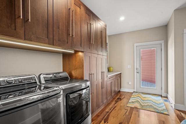 laundry room featuring light wood-type flooring, washing machine and dryer, and cabinets