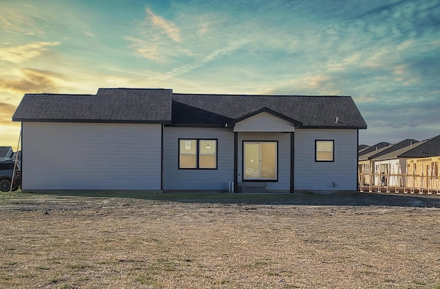 back house at dusk featuring a lawn