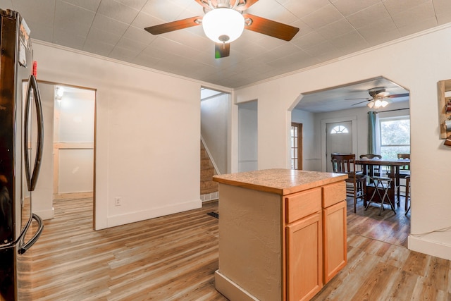 kitchen featuring a center island, stainless steel refrigerator, ornamental molding, light wood-type flooring, and ceiling fan