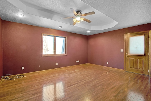 spare room featuring hardwood / wood-style flooring, a textured ceiling, a raised ceiling, and ceiling fan