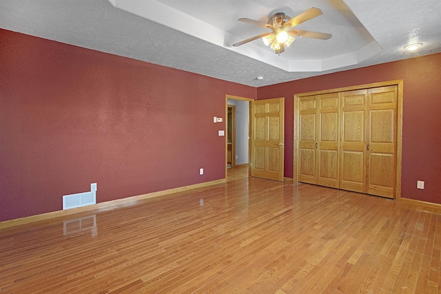 unfurnished bedroom with light hardwood / wood-style flooring, ceiling fan, a textured ceiling, a raised ceiling, and a closet