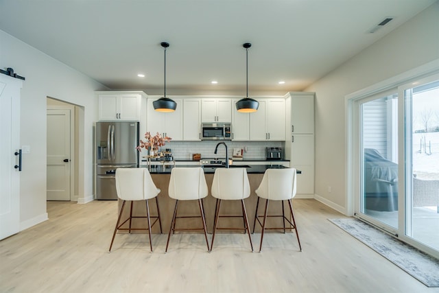 kitchen with appliances with stainless steel finishes, a barn door, hanging light fixtures, and white cabinets