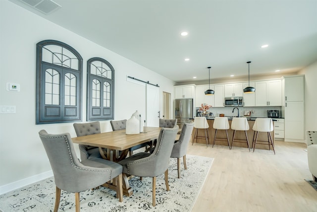 dining area with a barn door, sink, and light hardwood / wood-style floors