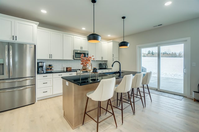 kitchen with sink, decorative light fixtures, stainless steel appliances, a kitchen island with sink, and white cabinets