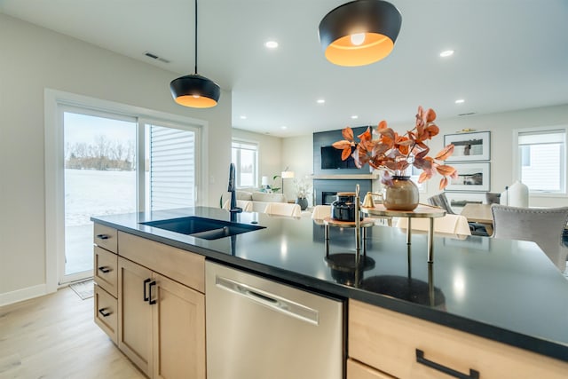 kitchen featuring a fireplace, sink, hanging light fixtures, stainless steel dishwasher, and light hardwood / wood-style flooring