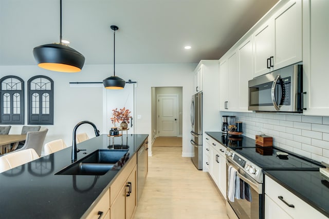 kitchen with appliances with stainless steel finishes, sink, white cabinets, hanging light fixtures, and a barn door