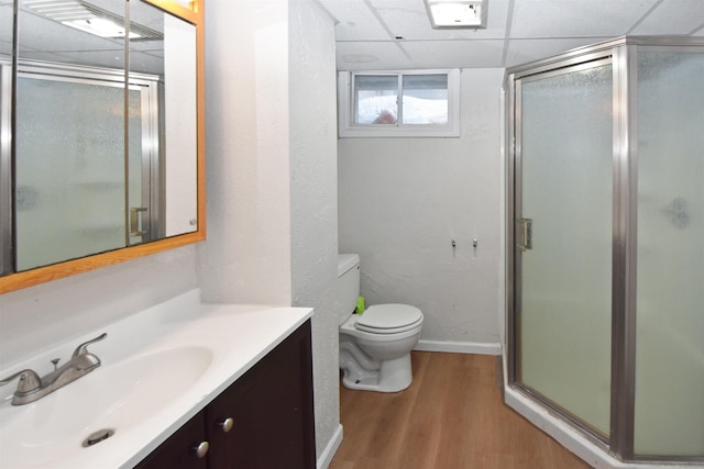 bathroom featuring a paneled ceiling, vanity, wood-type flooring, a shower with shower door, and toilet