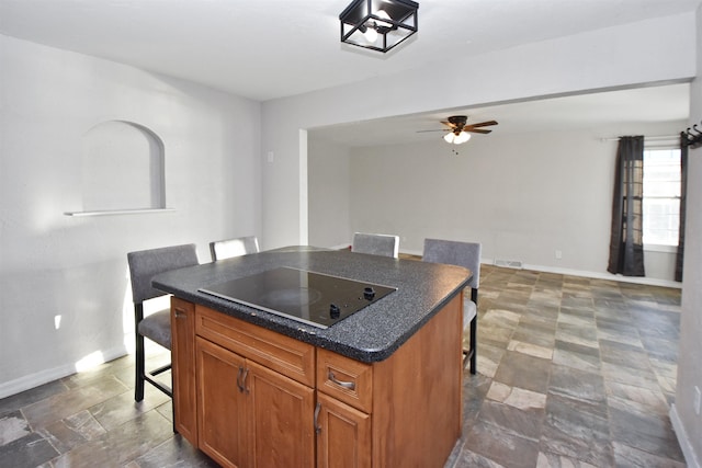 kitchen with black electric cooktop, ceiling fan, a kitchen breakfast bar, and a center island