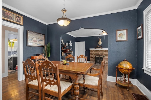 dining room featuring ceiling fan, ornamental molding, dark hardwood / wood-style flooring, and a brick fireplace