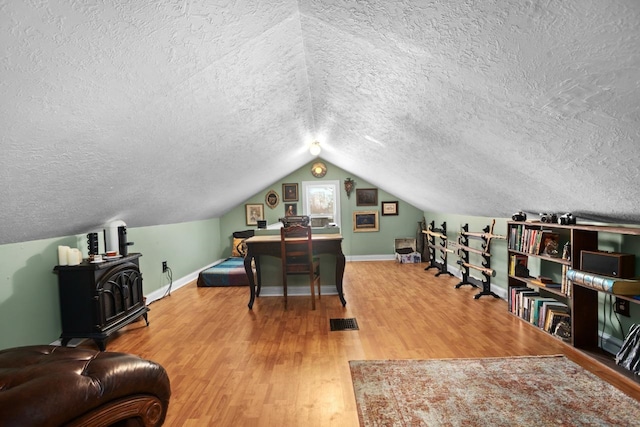 office area with wood-type flooring, lofted ceiling, a wood stove, and a textured ceiling