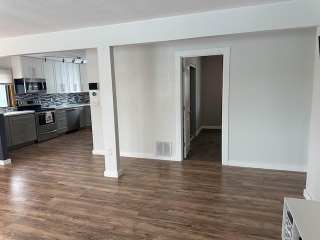 kitchen with dark wood-type flooring, a textured ceiling, appliances with stainless steel finishes, gray cabinets, and backsplash