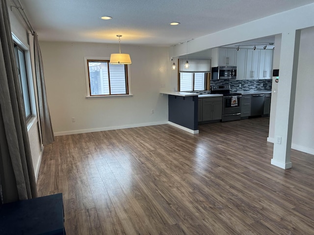 kitchen with pendant lighting, backsplash, dark hardwood / wood-style flooring, kitchen peninsula, and stainless steel appliances