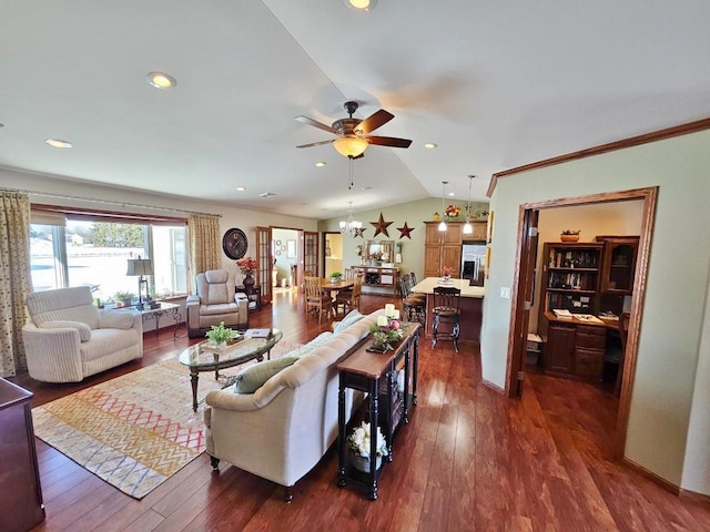 living room featuring dark wood-type flooring, lofted ceiling, crown molding, and ceiling fan with notable chandelier