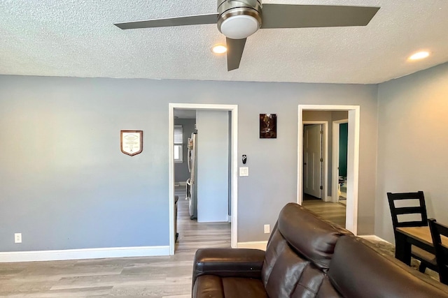 living room with ceiling fan, a textured ceiling, and light wood-type flooring