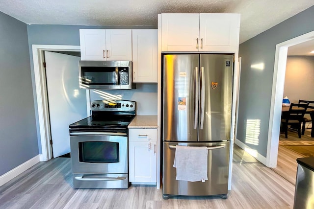 kitchen featuring a textured ceiling, stainless steel appliances, light hardwood / wood-style floors, and white cabinets