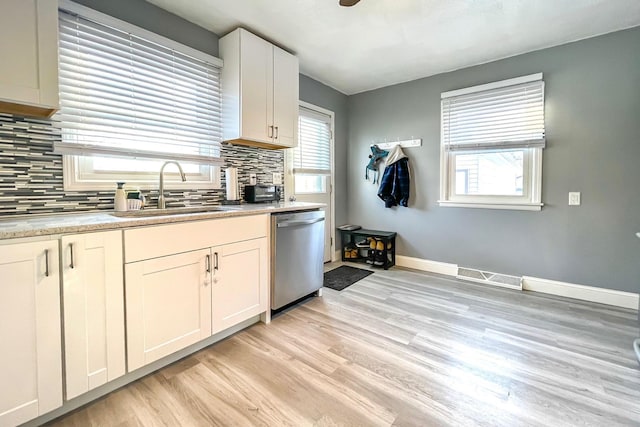 kitchen with tasteful backsplash, sink, white cabinets, stainless steel dishwasher, and light wood-type flooring