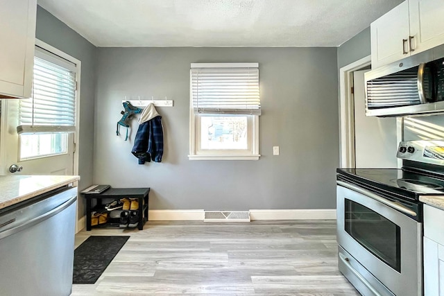 kitchen featuring appliances with stainless steel finishes, white cabinets, a textured ceiling, and light hardwood / wood-style flooring