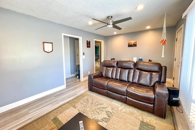 living room with ceiling fan, a textured ceiling, and light wood-type flooring