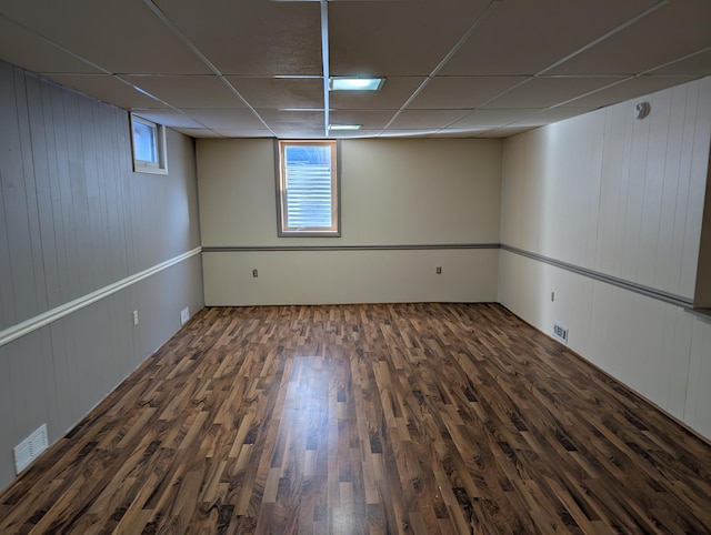 basement with dark wood-type flooring, a paneled ceiling, and a healthy amount of sunlight