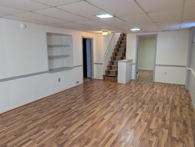 basement with dark wood-type flooring, a drop ceiling, and built in features