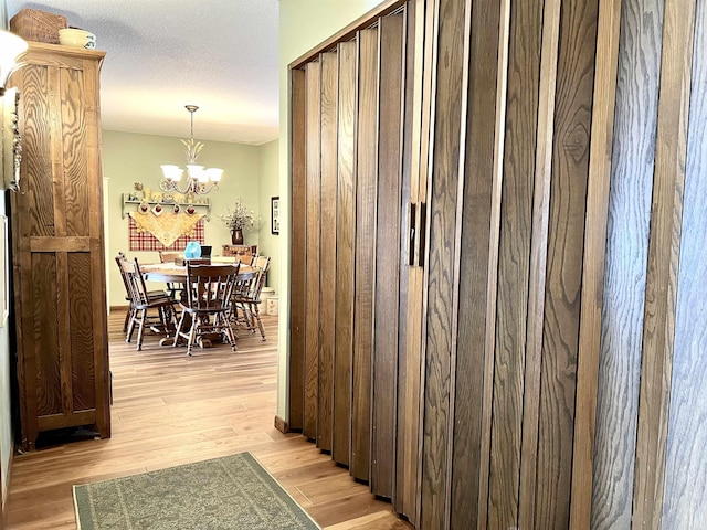 hall with an inviting chandelier, a textured ceiling, and light wood-type flooring