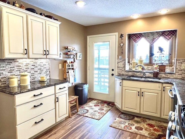 kitchen with sink, dark stone countertops, backsplash, a textured ceiling, and light hardwood / wood-style flooring