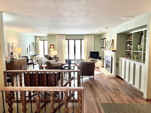 living room with built in shelves, a fireplace, hardwood / wood-style floors, and a textured ceiling