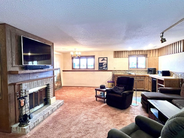 carpeted living room with rail lighting, a brick fireplace, a chandelier, and a textured ceiling