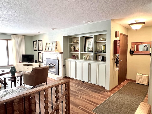 living room with a brick fireplace, wood-type flooring, and a textured ceiling