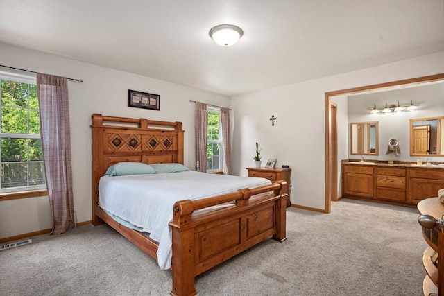 carpeted bedroom featuring ensuite bathroom, sink, and multiple windows