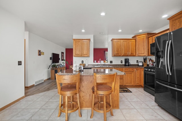 kitchen with sink, a breakfast bar, a center island, light stone countertops, and black appliances