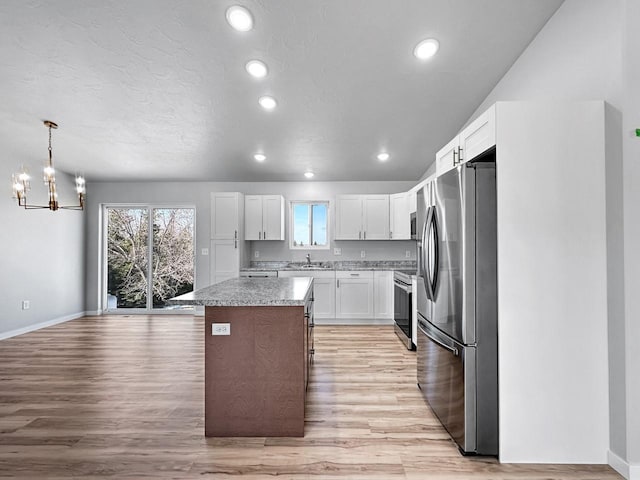 kitchen with a kitchen island, appliances with stainless steel finishes, decorative light fixtures, white cabinetry, and sink