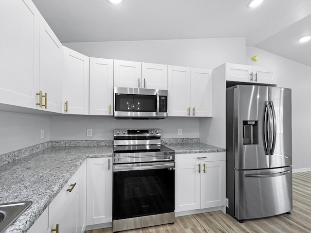 kitchen featuring white cabinetry, light stone counters, vaulted ceiling, light hardwood / wood-style flooring, and appliances with stainless steel finishes
