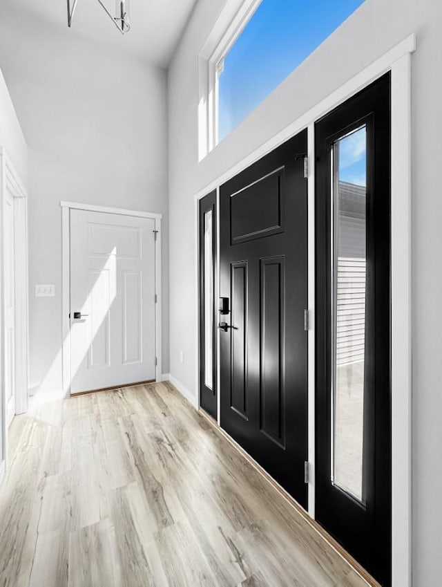 entryway with a towering ceiling, light hardwood / wood-style floors, and a chandelier