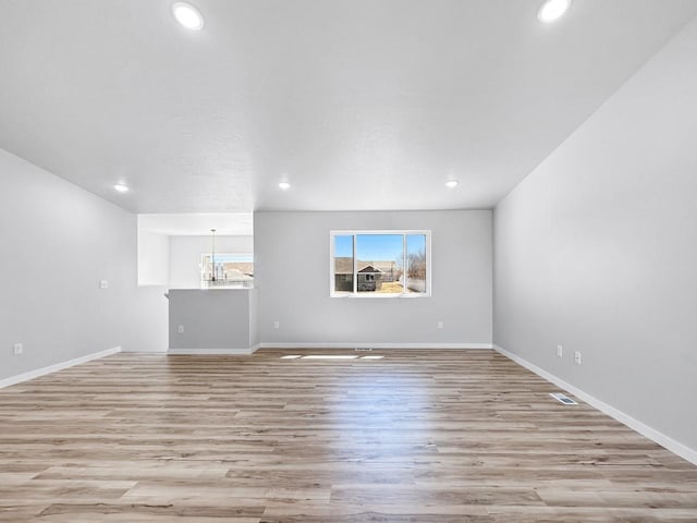 unfurnished living room with a chandelier and light wood-type flooring
