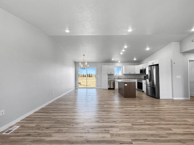 kitchen featuring pendant lighting, appliances with stainless steel finishes, white cabinetry, a kitchen island, and vaulted ceiling