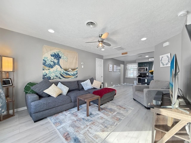 living room with a textured ceiling, light wood-type flooring, and ceiling fan