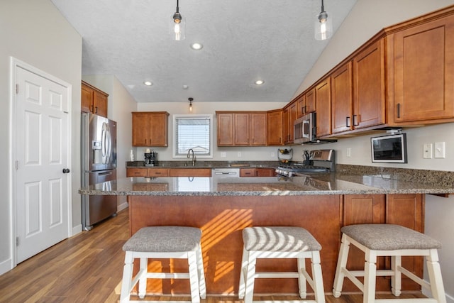 kitchen featuring a peninsula, brown cabinets, appliances with stainless steel finishes, and a breakfast bar