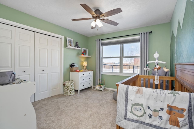 bedroom with a closet, light colored carpet, ceiling fan, a textured ceiling, and a nursery area